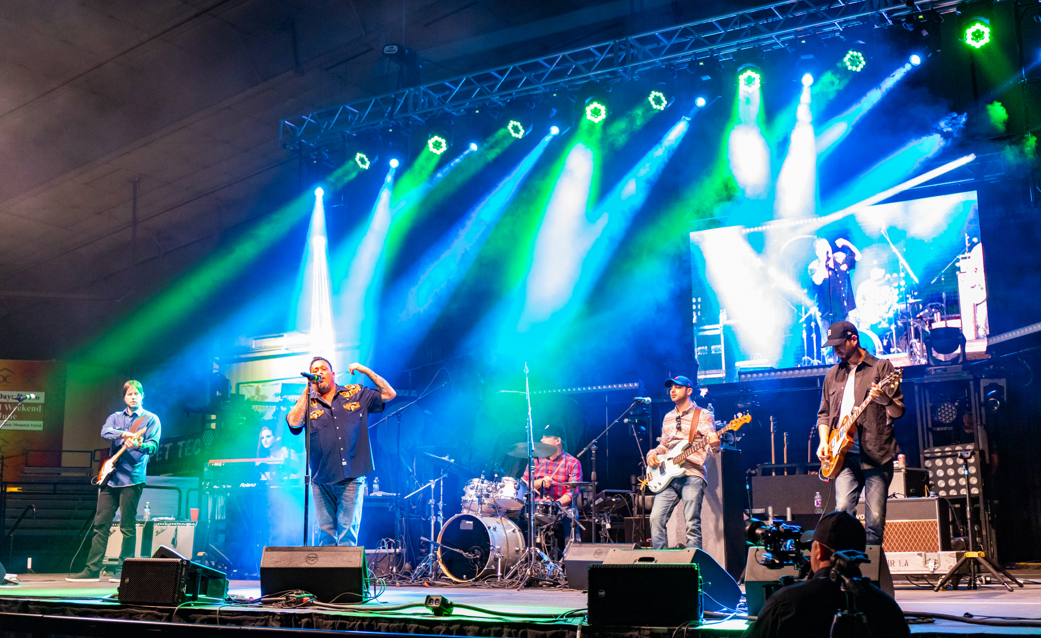 A band performs on a stage surrounded by speakers and bright shafts of light