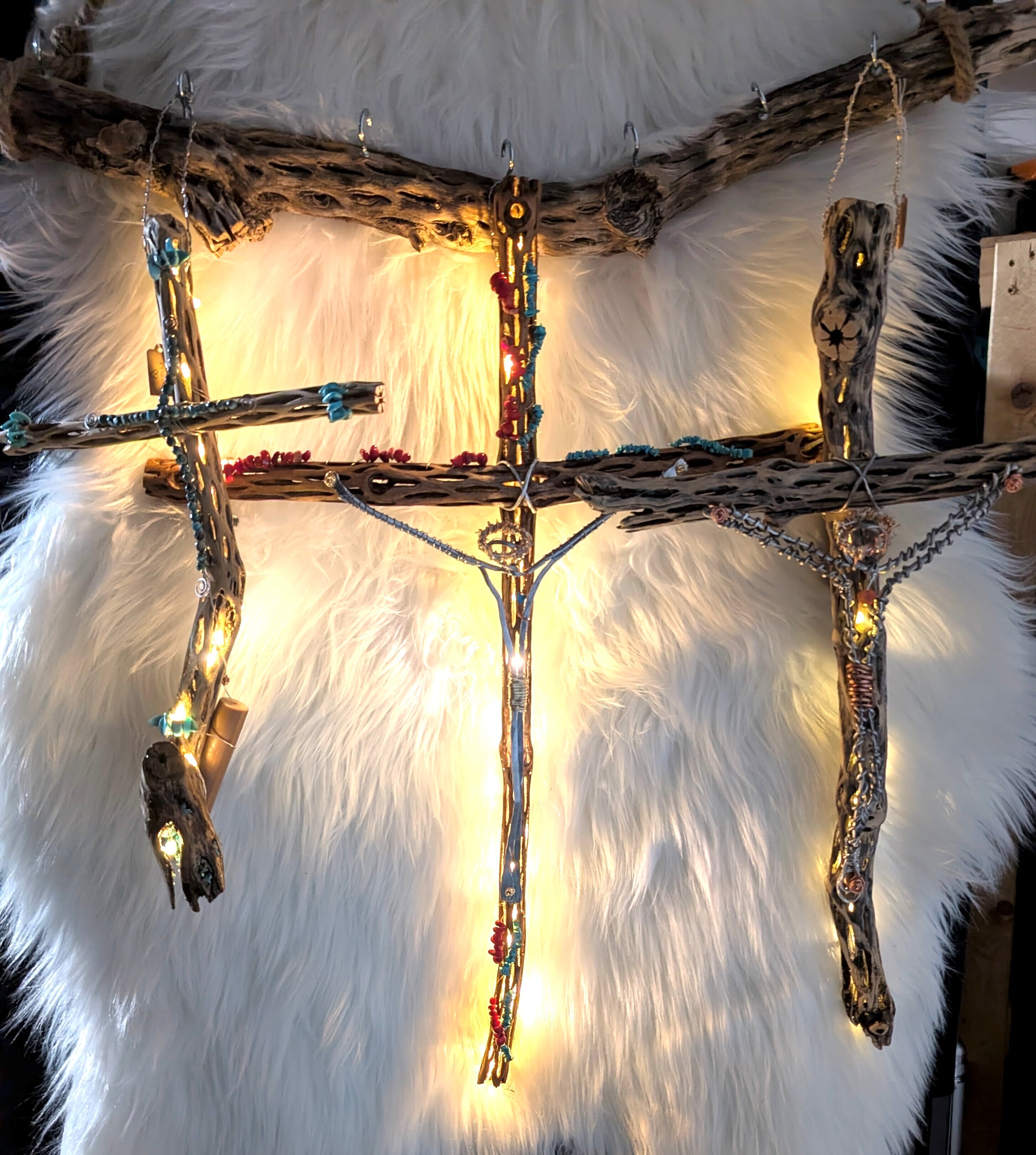 Chola crosses with embedded string lights hang against a white fur background. The central cross is adorned with colorful beads and stones.