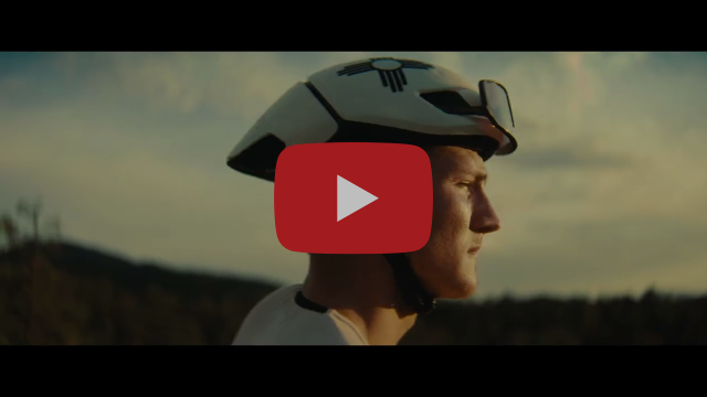 Profile of a person wearing a bicycle helmet with sunglasses in front of shadowed hills and a cloudy sky