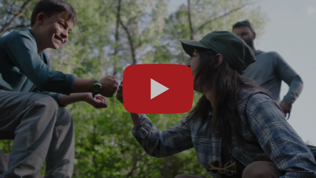 A person bumping fists with a young person in a wooded area