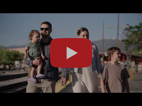 A family of four walks next to a set of railroad tracks with trees and lightposts in the background