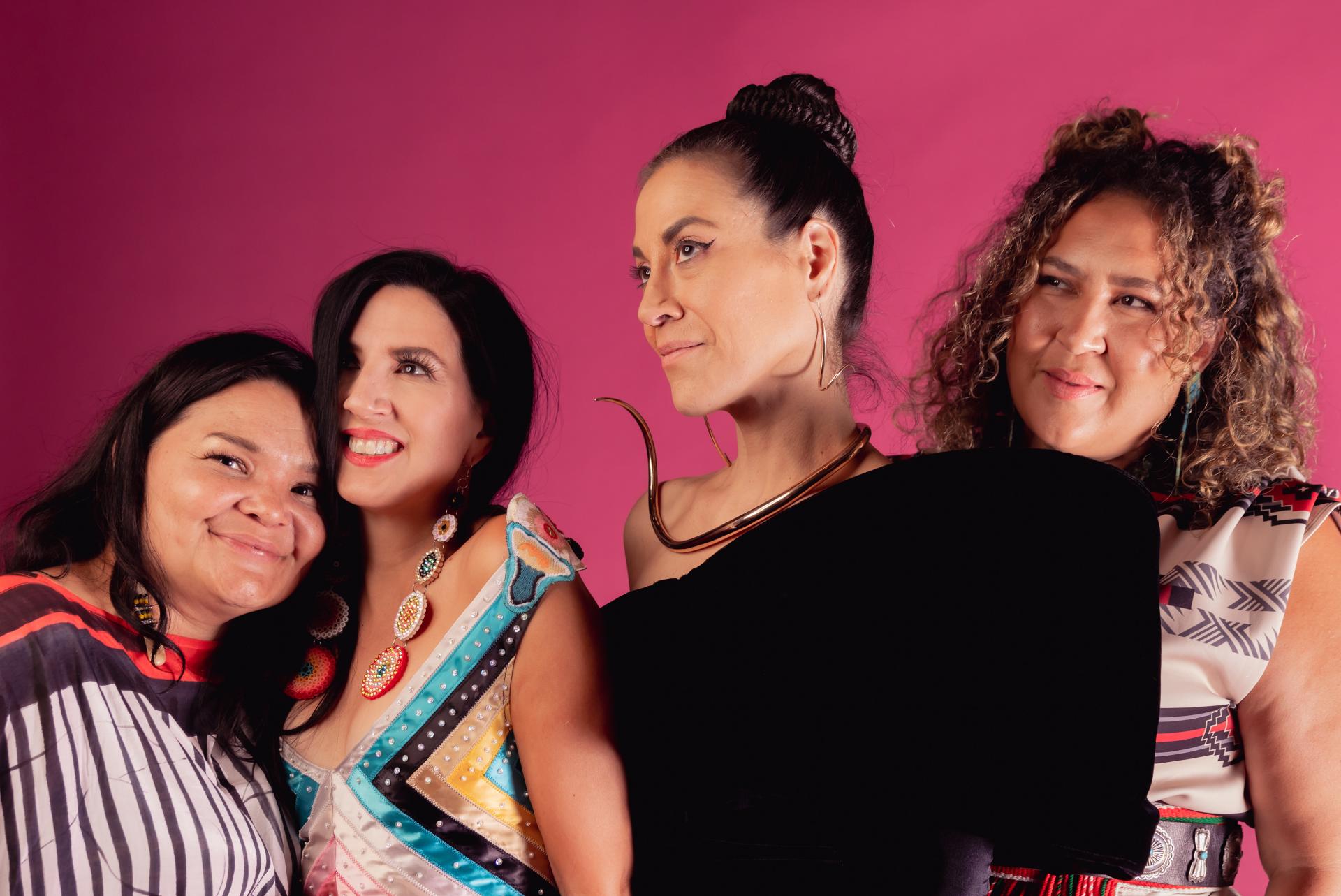 Four people in different patterned and intricate outfits stand in front of a colorful backdrop