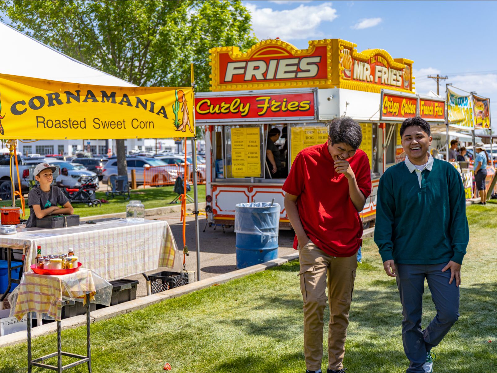 Two people laughing a smiling while walking away from a row of different food trucks and tents at an event.