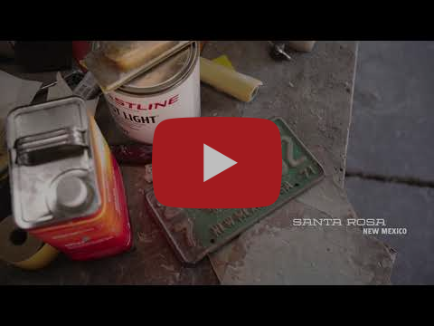 Cans of different chemicals sit on a dusty workbench next to a historic New Mexico license plate