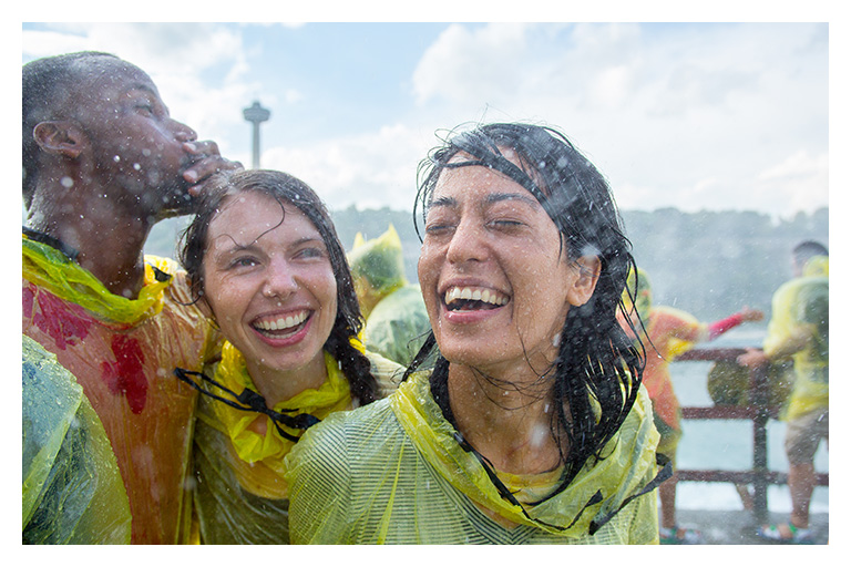 Friends in yellow ponchos laugh together as mist from Niagara Falls splashes around them on a lively spring visit.
