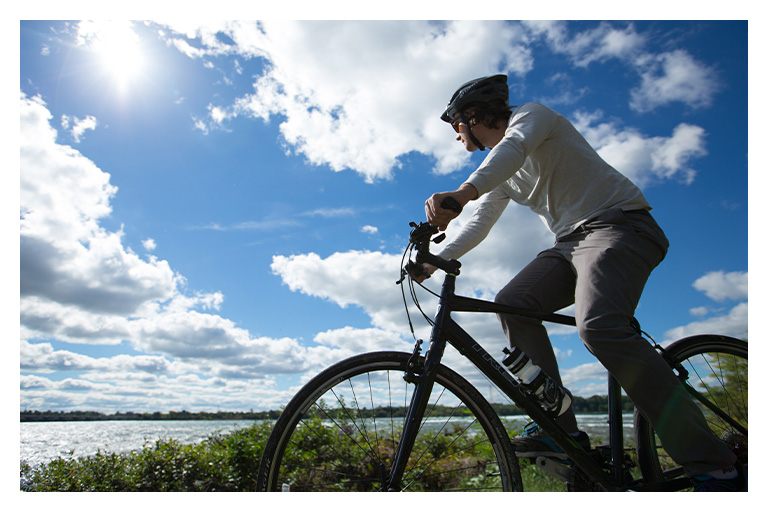 A cyclist rides along a scenic waterfront trail under bright blue skies, enjoying an active spring day near Niagara Falls.