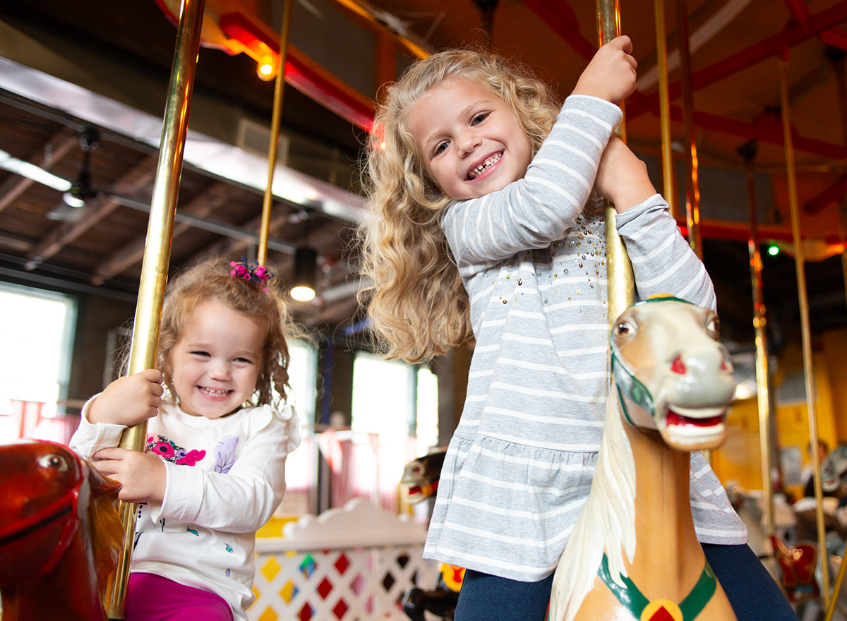 Two young children smile while riding a carousel, capturing the fun and family-friendly experiences available in Niagara Falls.