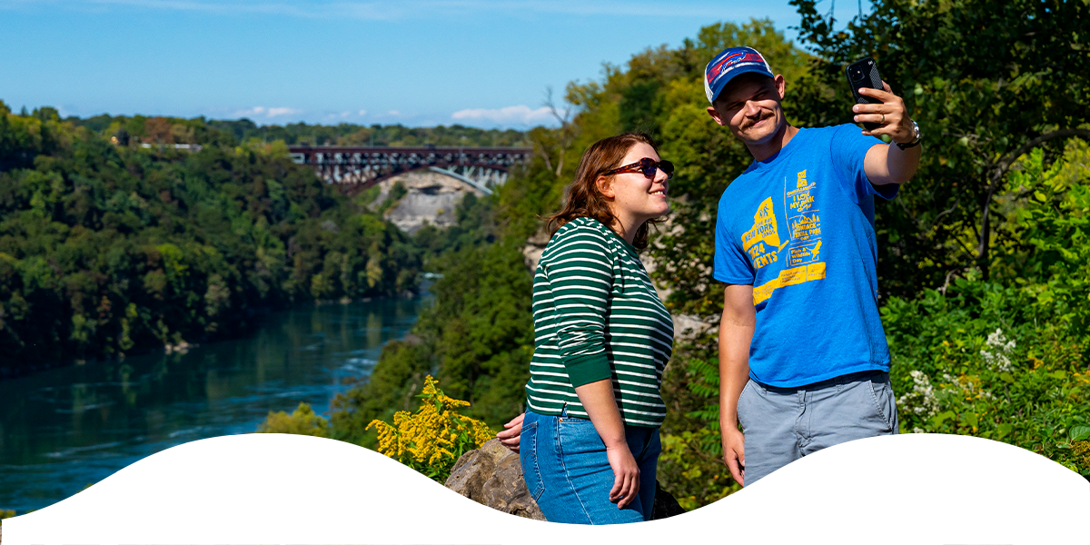 Couple taking a selfie at a scenic overlook above the Niagara River gorge on a sunny day.