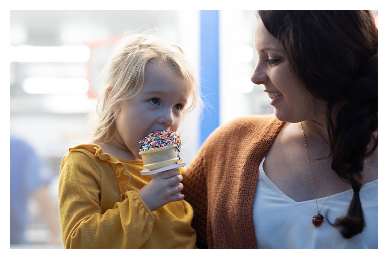 Young child enjoying a colorful ice cream cone while smiling at a parent during a family outing.