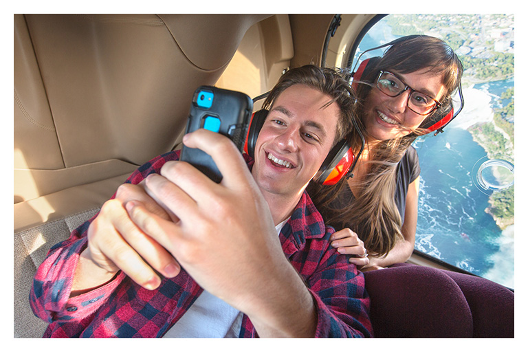 Couple wearing headsets takes a selfie during a helicopter tour above Niagara Falls and the Niagara River.