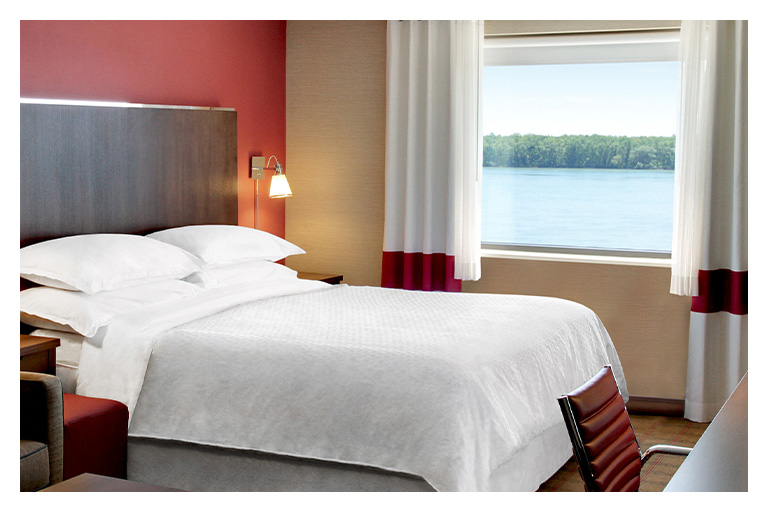 Bright hotel room with a king bed and large window overlooking the Niagara River, offering a relaxing overnight stay.