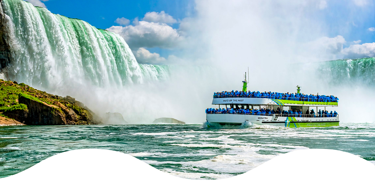 Maid of the Mist boat cruises beside the towering Horseshoe Falls, surrounded by mist and rushing water on a sunny day.