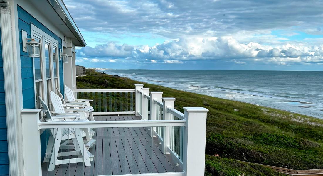 A picturesque blue house with white chairs on the porch, overlooking the beautiful ocean scenery