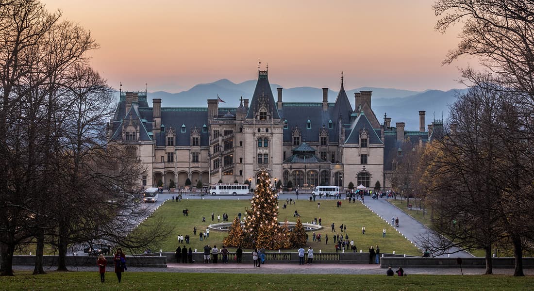View of front of Biltmore Estate with Christmas tree lit up in front and people walking around during sunset