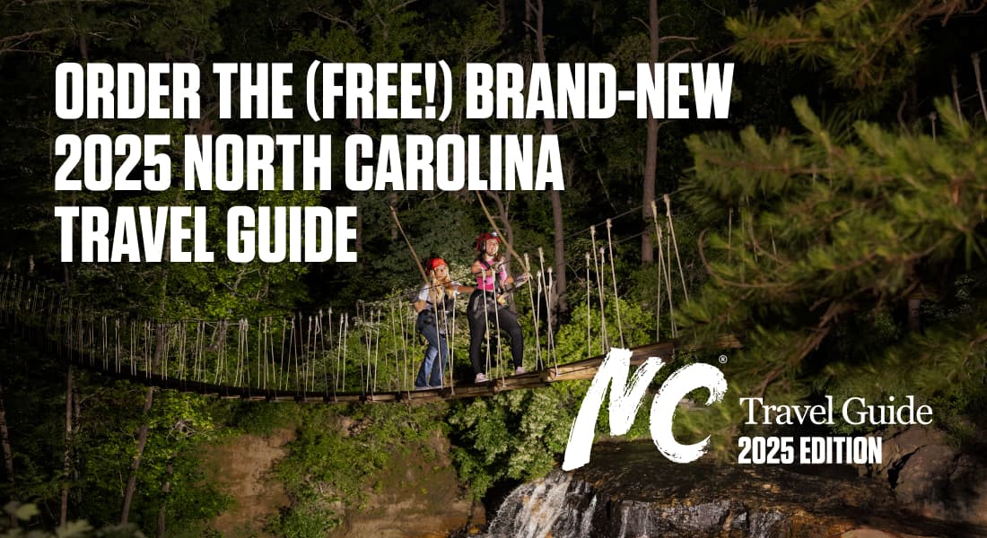 ORDER THE (FREE!) BRAND-NEW 2025 NORTH CAROLINA TRAVEL GUIDE - Two women crossing a bridge over a waterfall at ZipQuest in Fayetteville