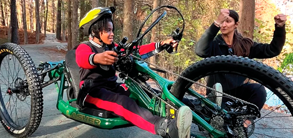 A child rides a sit bike with an instructor helping with technique.  
