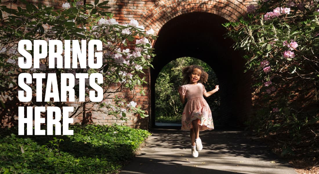 SPRING STARTS HERE - Little girl happily skipping from out of a brick tunnel on the grounds of Biltmore Estate, with beautiful spring flowers around her