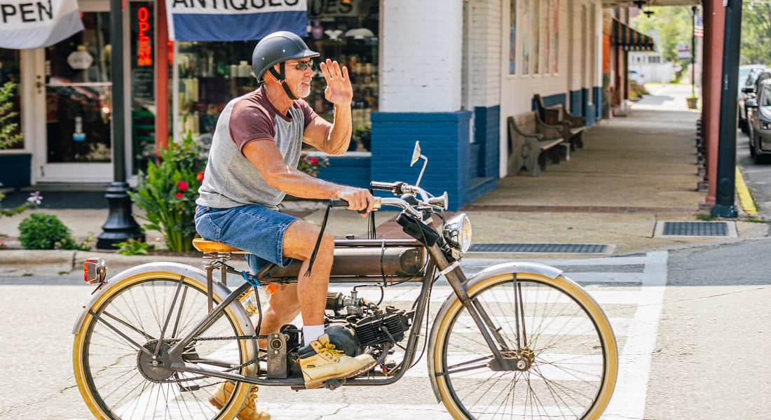 Cyclist on a vintage motor bicycle waves as he passes Treasury Antiques along Raiford Street in Selma