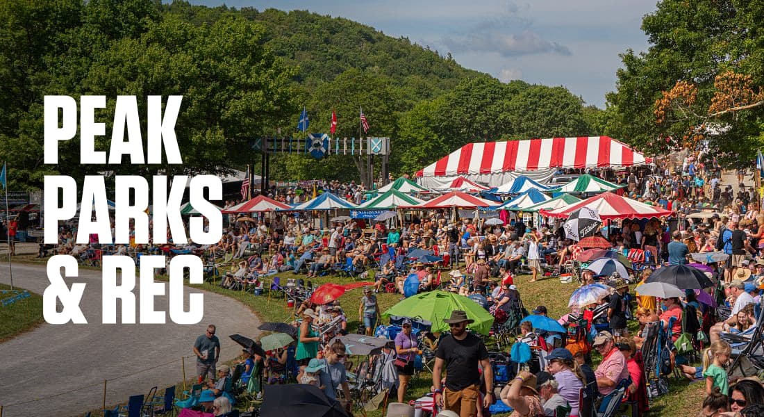 PEAK PARKS & REC - large crowd of people sitting on lawn watching Highland Games, with tents and trees in background outdoors during daytime