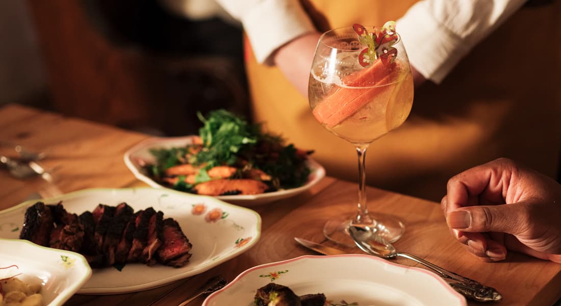 A table set with plates of grilled meat, salad, and a cocktail, Supperland restaurant Charlotte NC