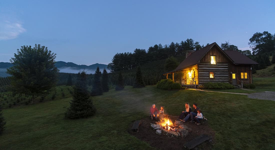 Family sitting around a campfire in front of a log cabin. Boyd Mountain, NC