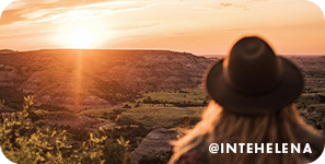 person standing over looking landscape with sun setting in background