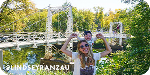 woman iwth small child on shoulders smiling with bridge and river in background