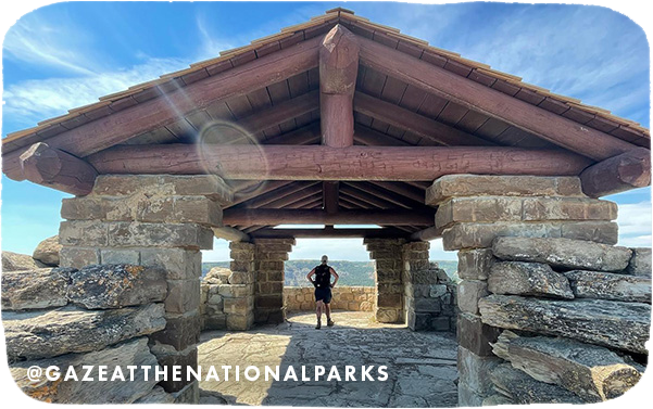 Person standing under a large wood and stone shelter at a national park