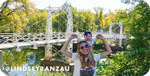 Woman holding a baby while standing in front of a white bridge and water
