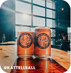 Two orange beer cans sitting on a table in front of a glass garage door at a brewery, with overlay text that reads @kattellsall
