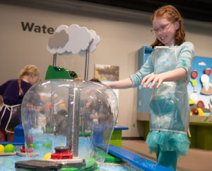A red-headed young girl interacting with a weather-related exhibit at a science center