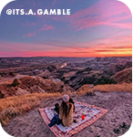 A woman sitting on a blanket overlooking a beautiful pink sunset, with overlay text that reads @its.a.gamble