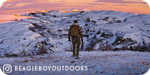 View from behind of a man trekking through snow with snowy mountains and a pink sunset ahead of him, with overlay text that reads beagleboyoutdoors