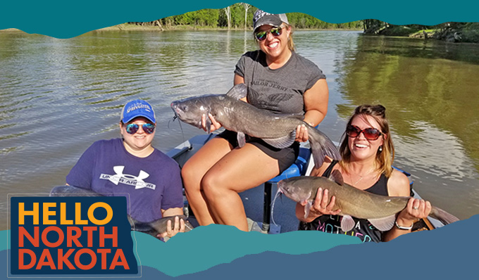 Three women on a boat smiling and holding large catfish, with overlay text that reads: Hello North Dakota