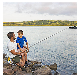 Man and young boy on the rocky shore of a lake with a fishing rod