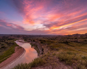 A beautiful pink and purple sky and clouds at sunset above a river and open green space