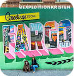 A woman and a dog posing in front of a colorful mural that reads 