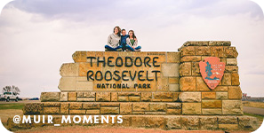 Woman and two children sitting on top of a sign made out of stones that reads 
