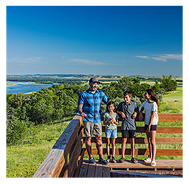 Man and three kids standing on a wood lookout point with trees and water behind them