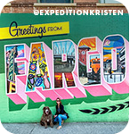A woman and a dog posing in front of a colorful mural that reads 