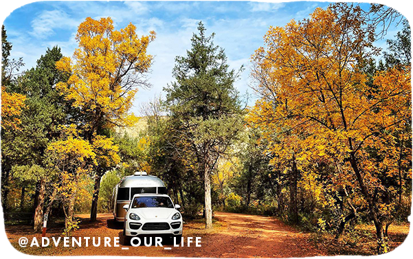 A white car and silver trailer parked and surrounded by trees with gold fall leaves, with overlay text that reads: @adventure_our_life