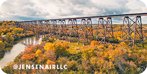 Bridge spanning over a river surrounded by colorful gold and orange trees, with overlay text that reads: @jensenairllc