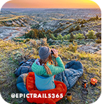 Woman sitting outside looking through binoculars at a valley and sunset below her, with overlay text that reads: @epictrails365