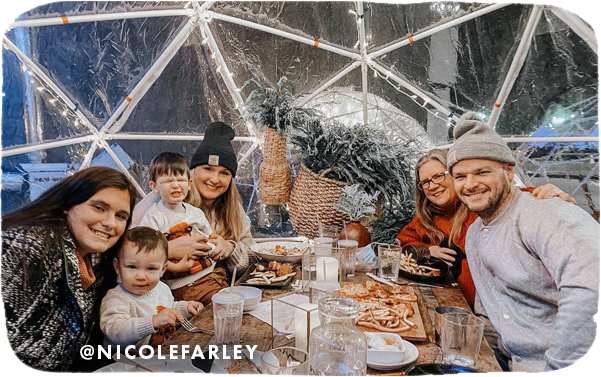 A group of three women, a man and three young boys eating at a table inside a plastic dome with holiday lights on it, with overlay text that reads: @nicolefarley