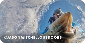 View from below the surface of a frozen lake of a man pulling a fish out of a hole, with overlay text that reads: @jasonmitchelloutdoors