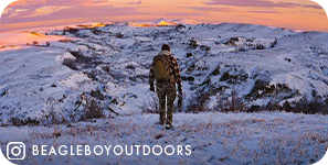 View from behind of a person walking on snowy ground with snowy mountains and a pink sky ahead of them, with overlay text that reads: @beagleboyoutdoors