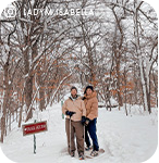 A couple standing in a snowy forest on snowshoes, with overlay text that reads: @ladymisabella