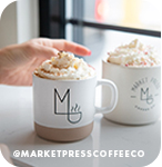 Hand reaching for two mugs of coffee beverages topped with whipped cream, with overlay text that reads: @marketpresscoffeeco