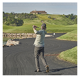View from behind of a man swinging a golf club, with rolling greens hills of a golf course in the background