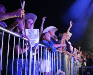 Crowd of kids behind a metal barrier enjoying a concert